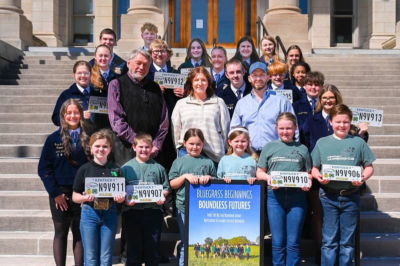 Group of Kentucky FFA students standing on stairs while holding Kentucky agriculture license plates with FFA Logo on them