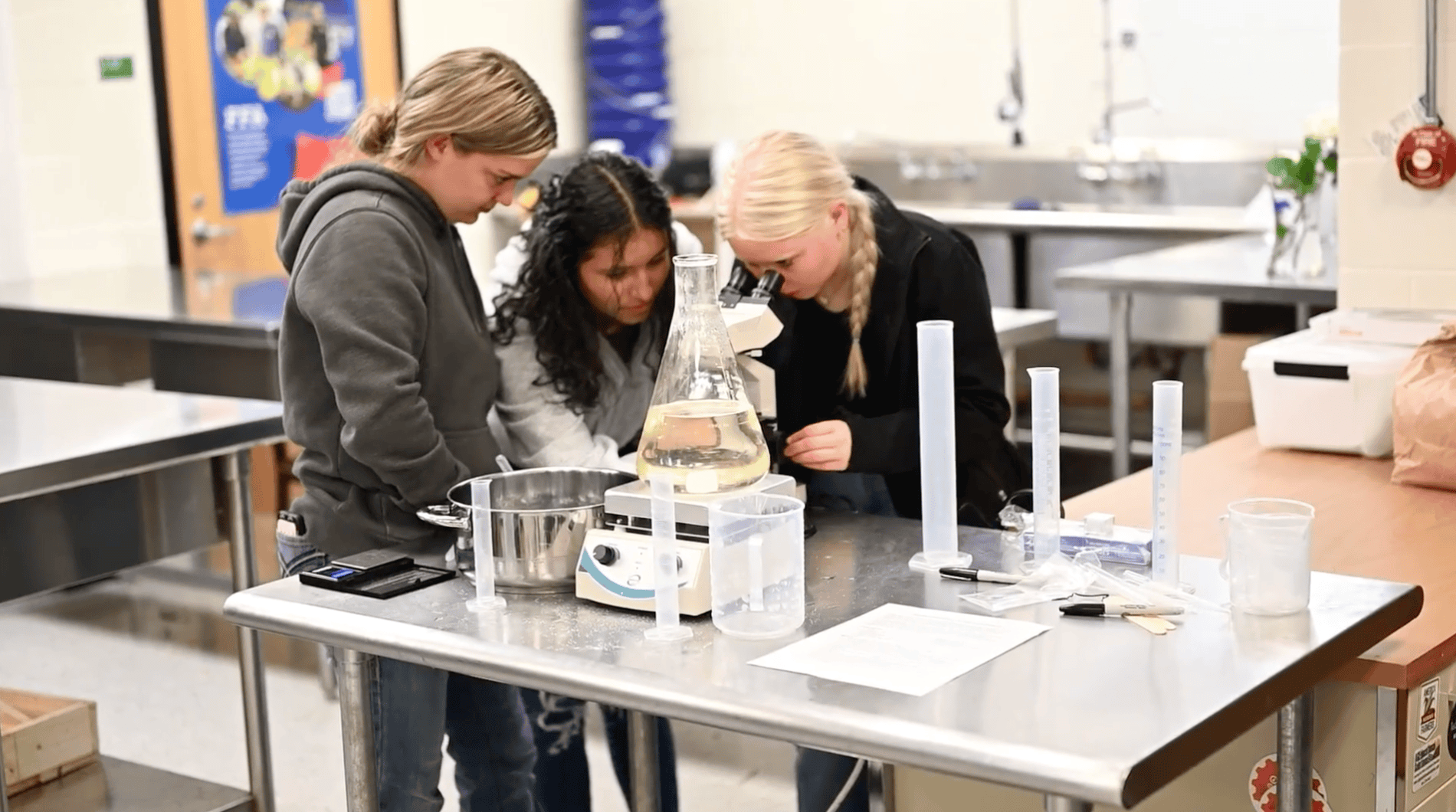 3 female students in classroom looking in a microscope